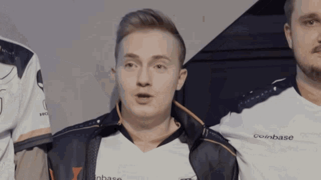 a man wearing a coinbase shirt stands with two other men