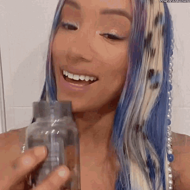 a woman with blue and white hair is smiling while holding a bottle .