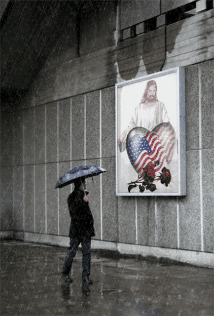 a man with an umbrella stands in front of a painting of jesus holding an american flag