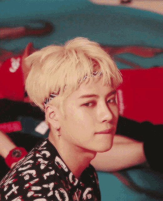 a young man with blonde hair wears a headband and earrings