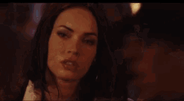 a close up of a woman 's face in a dark room with a fire in the background .