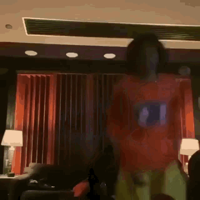 a man in an orange shirt is dancing in a living room with a couch and lamps .