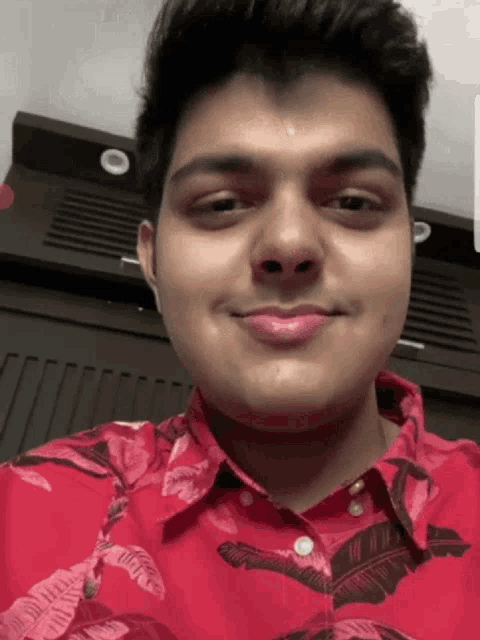 a young man wearing a red shirt with leaves on it is smiling