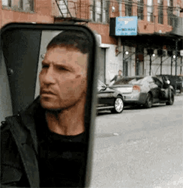 a man is looking at himself in a rear view mirror while standing on a city street .