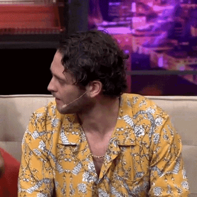 a man in a yellow shirt is sitting on a couch with a microphone in his mouth .