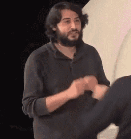 a man with a beard is shaking hands with another man while wearing a black jacket .