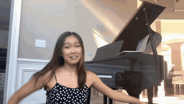 a girl in a black and white polka dot dress is standing in front of a piano