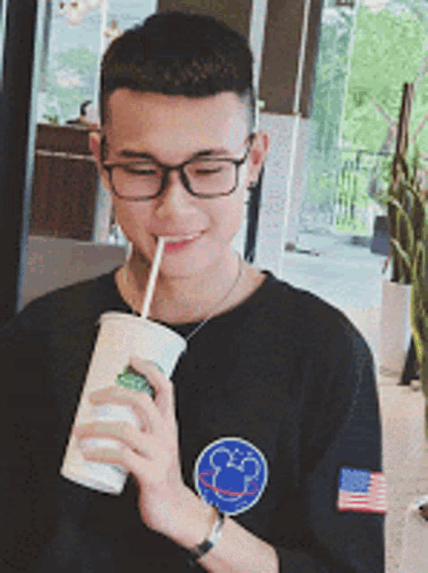 a young man wearing glasses is drinking from a cup through a straw