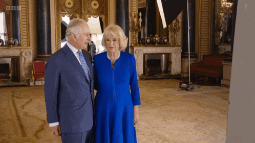 a man in a suit and tie stands next to a woman in a blue dress with bbc written on the bottom right