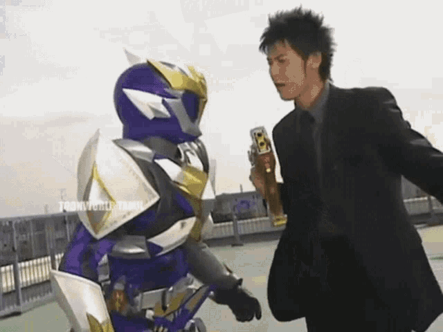 a man in a suit is standing next to a superhero in a blue armor .