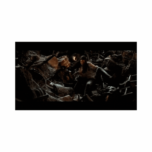 a woman in a white dress is standing in a pile of rubble in a dark room .
