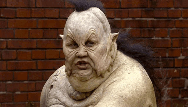 a statue of a monster with a mohawk stands in front of a red brick wall