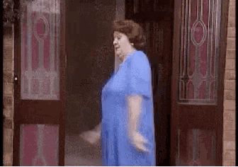 an older woman in a blue dress is standing in front of a door .