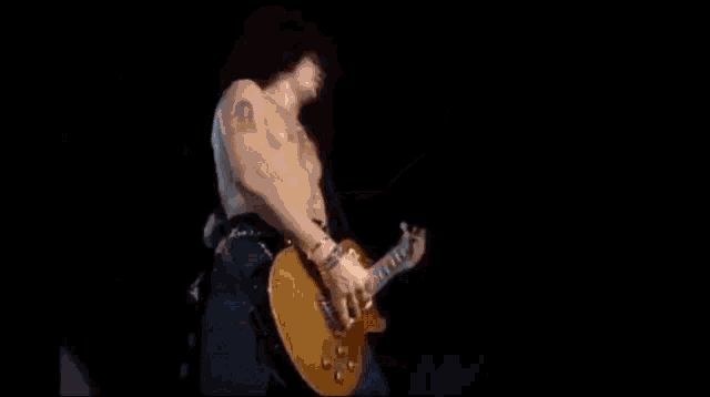 a shirtless man is playing a guitar on a stage in the dark .