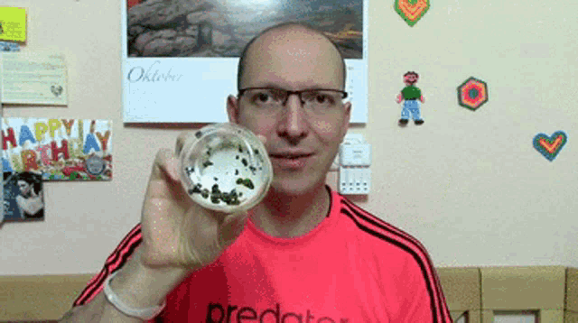 a man wearing a red predator shirt holds a container in his hand