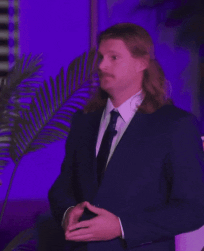 a man with long hair and a mustache is wearing a suit and tie .