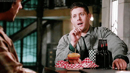 a man is sitting at a table eating a hamburger and drinking a beer .