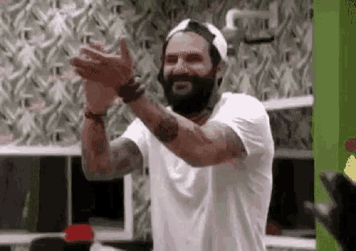 a man with a beard wearing a hat and a white shirt is clapping his hands .