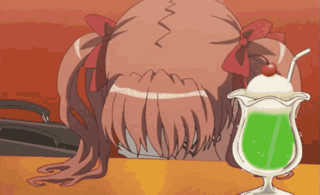 a girl sitting at a table with her head down next to a green drink