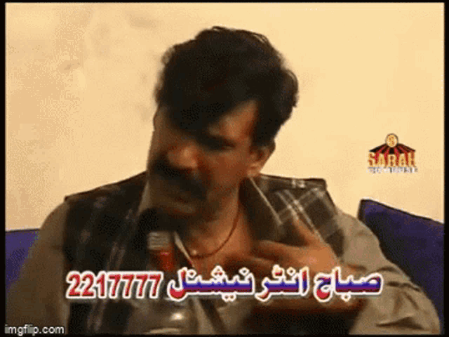 a man with a mustache is sitting on a couch talking on a cell phone