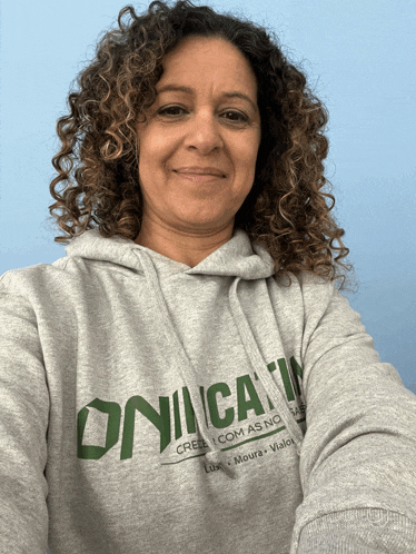 a woman with curly hair wears a grey hoodie that says onica