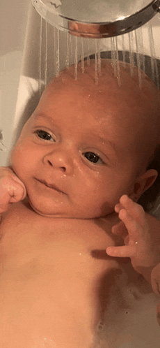 a baby is taking a shower in a bathtub and looking at the camera