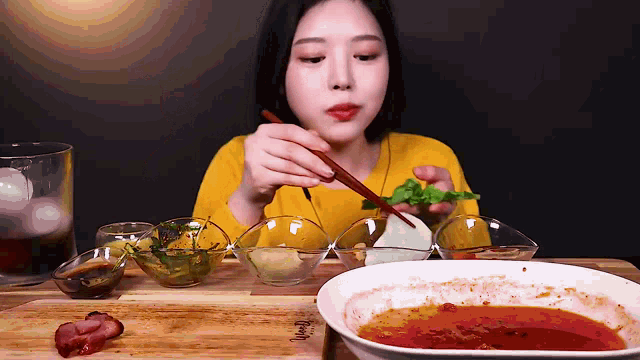a woman in a yellow shirt is eating something with chopsticks