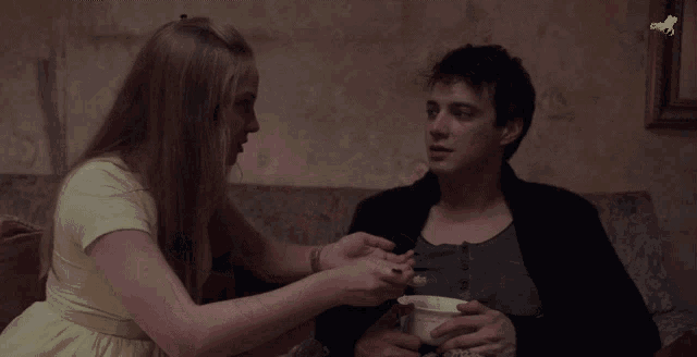 a woman is feeding a man a bowl of cereal with a picture of a horse on the wall in the background