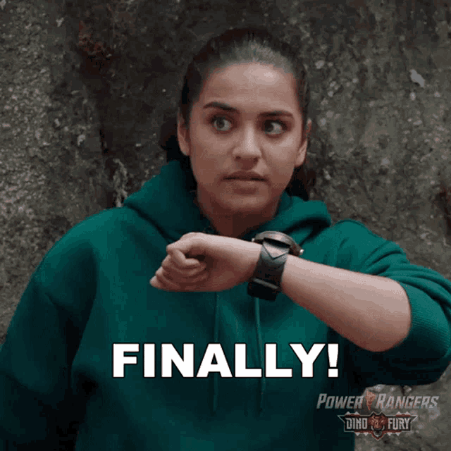 a woman wearing a green power rangers hoodie looks at her watch and says finally