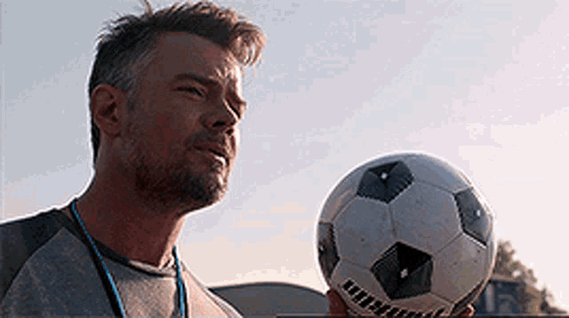 a man is holding a soccer ball in his hand and looking up at the sky .