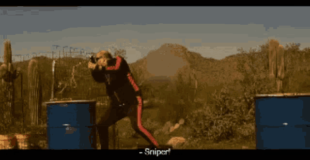 a man in a black jacket and red pants is holding a gun and says " sniper "