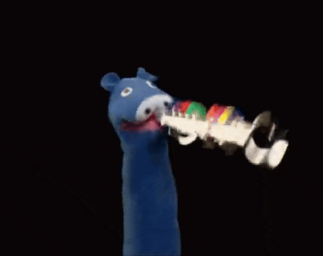 a blue puppet is holding a rainbow colored object in its mouth