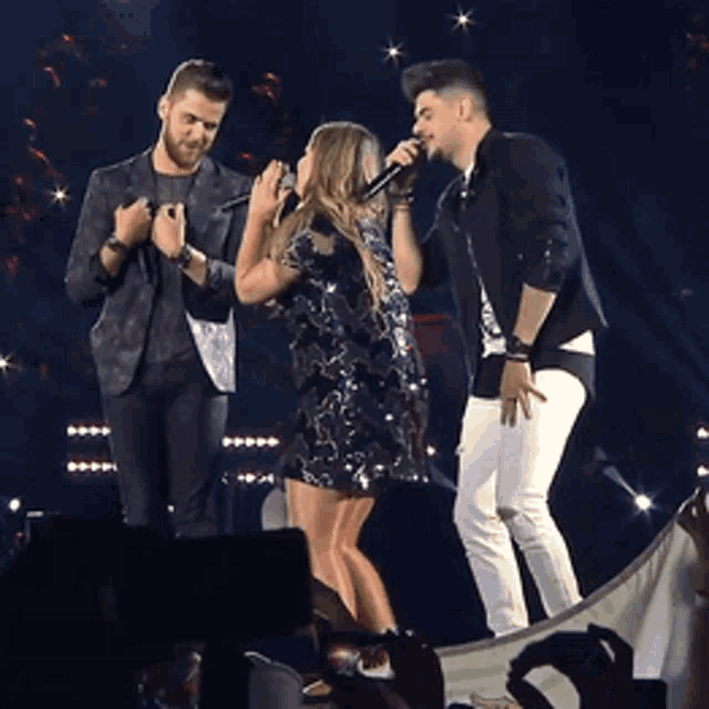a woman singing into a microphone with two men standing behind her
