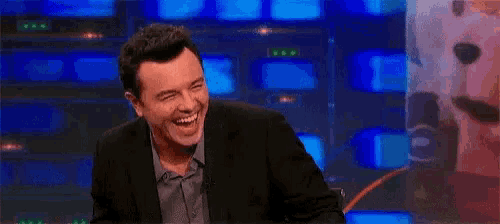 a man in a suit is smiling in front of a row of televisions