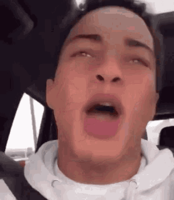 a young man is making a funny face while sitting in a car .