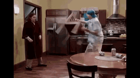 a man and a woman are standing in a kitchen fighting over a table .