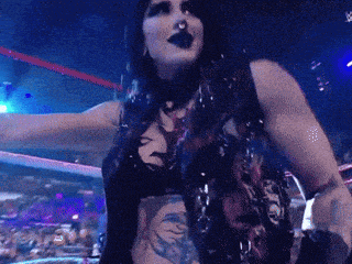 a woman in a wrestling ring with her arms outstretched and a tattoo on her chest