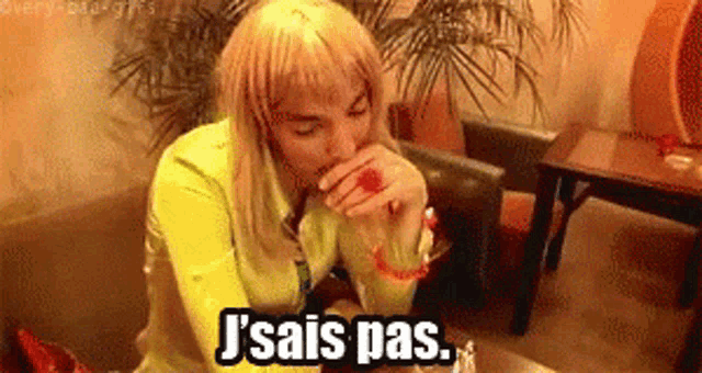 a woman with blonde hair is sitting at a table and says j'sais pas