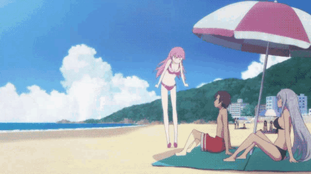 a girl in a bikini stands next to a boy sitting under an umbrella on a beach
