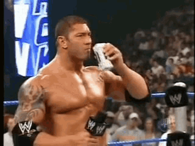a shirtless wrestler is holding a microphone and drinking from a can .