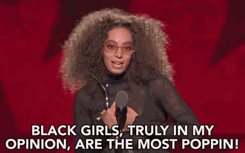 a woman with curly hair is speaking into a microphone and saying black girls truly in my opinion are the most poppin .