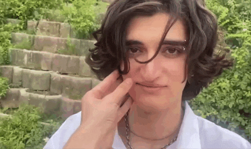 a man with long hair is touching his face with his finger .