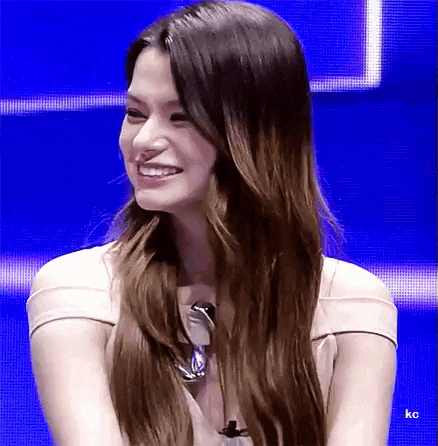 a woman with long hair is smiling while sitting in front of a blue screen .