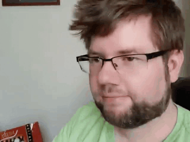 a man with a beard wearing glasses and a green shirt is looking at the camera .
