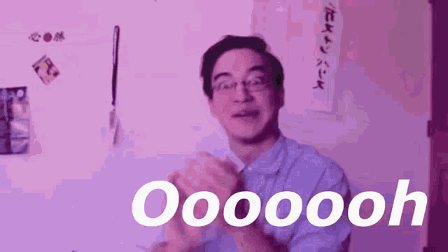 a man wearing glasses is clapping his hands in front of a wall that says oooooooh .