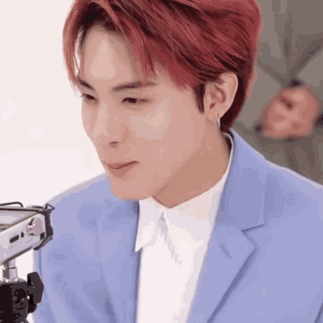 a young man with red hair is wearing a blue suit and white shirt and looking at a camera .