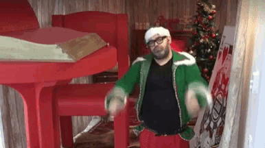 a man in an elf costume is dancing in a room with a christmas tree in the background