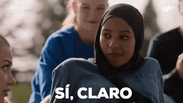 a woman in a hijab is standing in front of a group of people and says si claro .