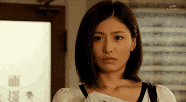 a woman with short hair is standing in front of a door holding a book and looking at the camera .
