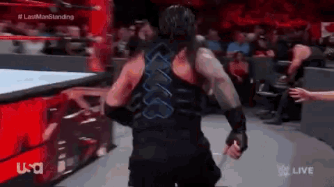 roman reigns is standing in the middle of a wrestling ring with a sword in his hand .